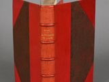 an old book with a red cover sitting on top of a table
