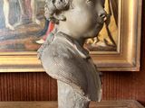 statue of a young boy in front of a painting on a wooden table