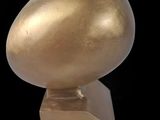 sculpture représentant un oiseau doré sur un socle, sur fond noir