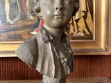 a bust of a young boy on a table in front of a painting