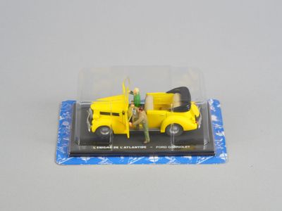 un petit camion jaune avec un homme debout à l'arrière