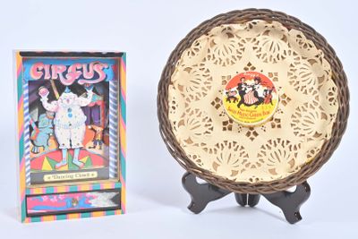 une assiette ornée d'une illustration, à côté d'une boîte de cartes de cirque