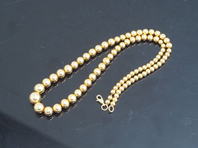 un gros plan d'un collier de perles dorées posé sur une surface noire