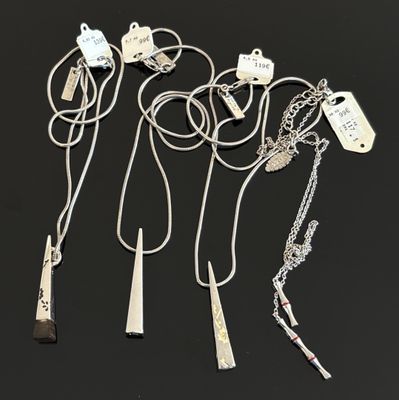 trois colliers en argent avec des pendentifs, posés sur un fond noir