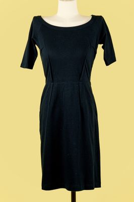 une robe noire posée sur un mannequin, sur fond jaune