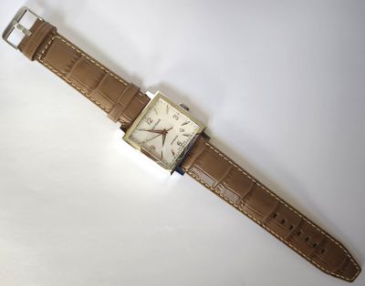 une image d'une montre sur une surface blanche avec un bracelet marron