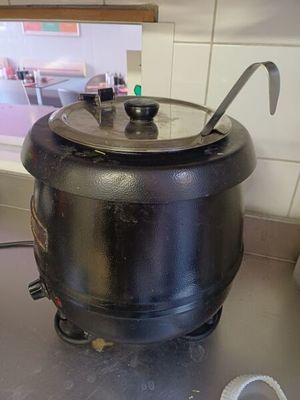 une casserole noire posée sur une cuisinière, avec une cuillère à l'intérieur