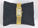 une image représentant une montre en or posée sur un coussin noir, sur une surface blanche
