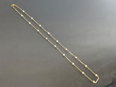 a long gold chain with white beads on a black surface