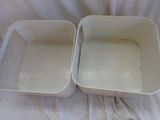 two white containers sitting on a bed with a white sheet