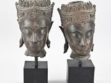 pair of bronze head vases on black stands on a white background