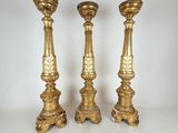 three gold candlesticks on a white surface with a white background