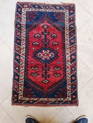 Tapis rectangulaire en laine à motif central sur fond rouge.