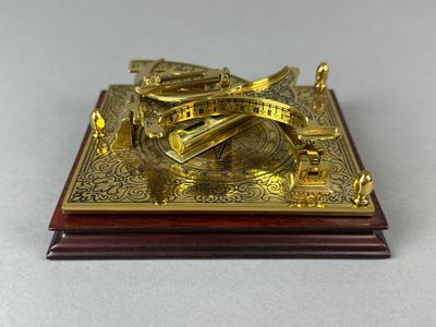 un cadran solaire plaqué or posé sur un socle en bois, posé sur une table