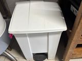 a white trash can sitting next to a toilet in a bathroom