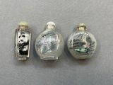 trois flacons à tabac en verre décorés de peintures, posés sur une table