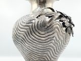 a silver vase that is sitting on a white surface