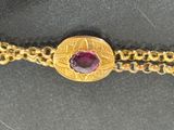 an image of a close up of a gold bracelet with a red stone
