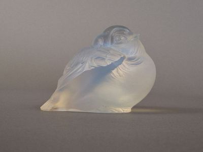 une figurine en verre dépoli représentant un oiseau, posée sur une table