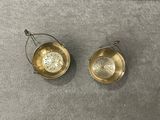 two small brass bowls with handles on a gray surface
