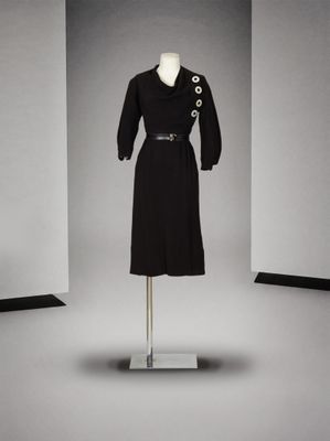 une robe noire avec des boutons et une ceinture, posée sur un présentoir pour mannequin