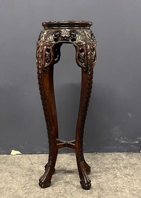 une table ancienne en bois, avec un plateau sculpté, posée sur un sol en ciment
