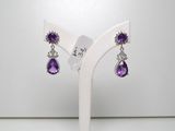 une paire de boucles d'oreilles violettes et blanches posées sur un présentoir blanc