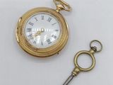 a gold pocket watch with a key attached to it