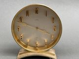 a gold clock that is on a stand on a table