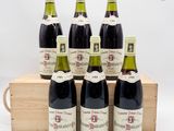six bouteilles de vin sont posées dans une caisse en bois sur une surface blanche
