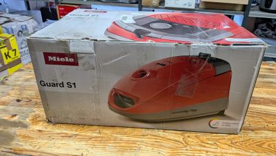 une boîte posée sur une table, dans laquelle se trouve une souris rouge