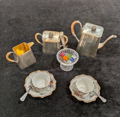 une théière en argent, des tasses et des soucoupes posées sur une table
