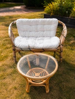 une chaise en osier et une table en verre dans l'herbe