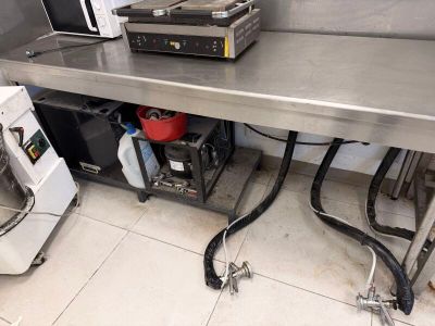 une grande table en inox dans une cuisine équipée d'un micro-ondes et d'un lave-vaisselle