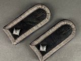 pair of black and silver embroidered badges on a gray surface