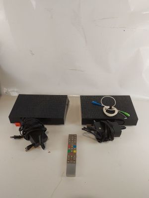 une paire d'enceintes noires, avec leurs câbles et leur télécommande, posées sur une surface blanche