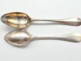 une paire de cuillères en argent posées sur une surface blanche, sur fond blanc