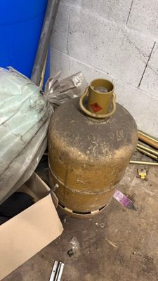 un sac rempli d'objets posé par terre à côté d'une bonbonne de propane