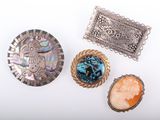 three silver brooches and two cameo brooches on a white surface