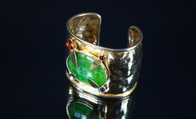 bague en argent ornée d'une feuille verte et de pierres rouges sur un fond noir