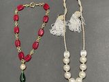 two necklaces with pearls and tassels on a table
