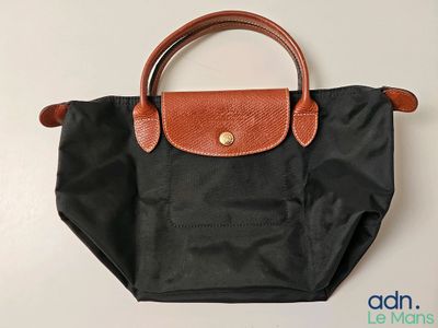 Le sac Longchamp est noir et possède une poignée marron.
