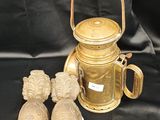 une théière en or et deux petites figurines posées sur un tissu noir