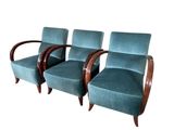 trois chaises bleues avec des accoudoirs en bois sont posées sur une surface blanche