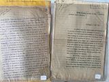 deux feuilles de papier ancien, couvertes d'écriture, posées sur une table