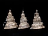 trois figurines en argent représentant des bouddhas assis sur une table