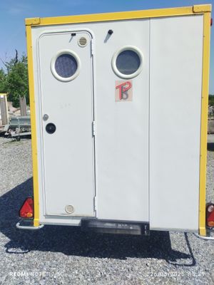 des toilettes portables blanches et jaunes installées sur un terrain recouvert de gravier