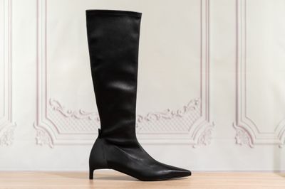des bottes en cuir noir montant jusqu'aux genoux, posées sur un parquet devant un mur blanc