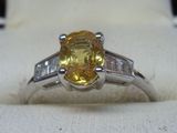 une photo d'une bague sertie d'un saphir jaune et de diamants, posée sur un tissu blanc