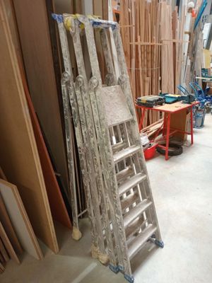une échelle appuyée contre un mur, à côté d'un tas de bois